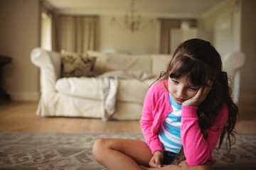 Naklejka premium School-age girl sitting cross-legged on patterned rug in living room by sofa, copy space