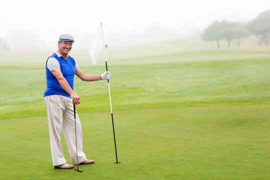Senior African American man standing on putting green gripping flagstick and golf club, copy space