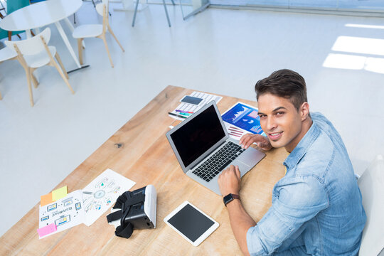 Mid adult man wearing denim shirt working on laptop with VR headset in office, copy space