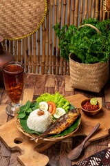 Fried skipjack tuna fish with rice, chilli sauce and vegetable. Serving on white plate on wooden table. Indonesian food and cuisine. Concept for whole healthy food, omega-3, animal protein.