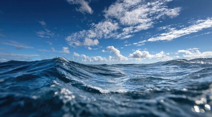 Fototapeta premium Ocean waves rolling under a vibrant blue sky filled with fluffy white clouds. The perspective is from a low vantage point, near the water's surface