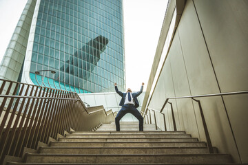 Happy business man with arms up standing in front of office buildings - Successful businessman celebrating victory outside