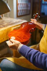 Skilled violinmaker carefully applying glossy varnish to wooden violin body, working meticulously...