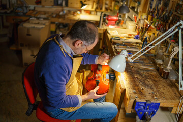 Skilled violinmaker carefully crafting wooden instrument, inspecting fine details under warm...