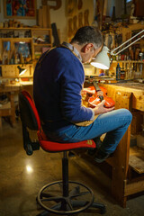 Fototapeta premium Skilled violinmaker carefully crafting wooden instrument, inspecting fine details under warm lighting, workshop filled with specialized luthier tools and raw materials