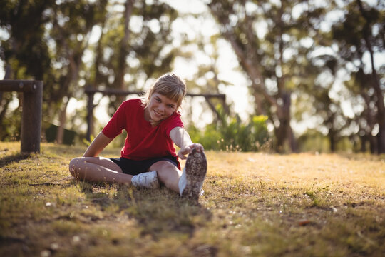 Fototapeta Teenage girl stretching hamstring in sunny park wearing red t-shirt, black shorts, white sneakers