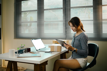 Young online seller checking order details on digital tablet in home office