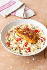 Orzo pasta with fried chicken breast, tomatoes and herbs. Italian food.