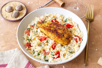 Orzo pasta with fried chicken breast, tomatoes and herbs. Italian food.