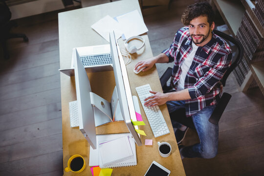 Bearded tech typing on keyboard at desk in office with dual monitors, headphones, server racks