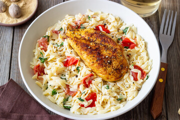 Orzo pasta with fried chicken breast, tomatoes and herbs. Italian food.