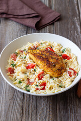 Orzo pasta with fried chicken breast, tomatoes and herbs. Italian food.