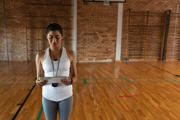 Athletic coach is holding tablet and wearing whistle on wooden basketball court under hoop © wavebreak3