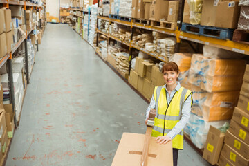 Female warehouse worker applying packing tape onto box in warehouse aisle with shelving, copy space