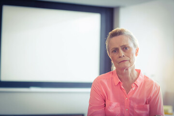 Senior woman looking thoughtful while sitting in meeting room with whiteboard, copy space