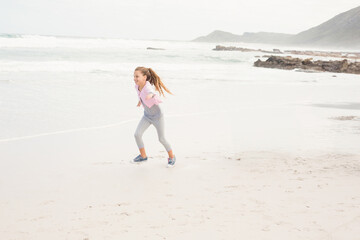 Girl running along wet sand at water's edge on beach wearing pink sportswear and sneakers