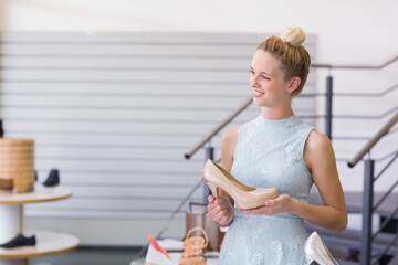 Female shopper examining beige patent leather pump inside footwear boutique with display tables