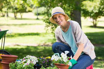 Adult woman gardener kneeling on pink pad in backyard arranging flowering plants in terracotta pots