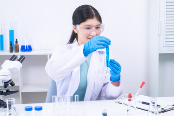 Young girl in goggles analyzing blue liquid sample in test tube during science experiment. Science,...