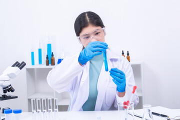 Young girl in goggles analyzing blue liquid sample in test tube during science experiment. Science,...