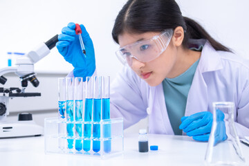 Teen scientist girl conducting science test by carefully evaluating blue solution in laboratory....