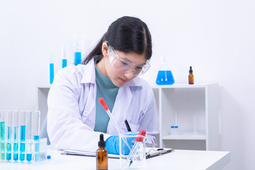 Asian female science student in lab coat writes notes in a laboratory notebook while analyzing...