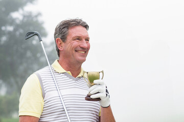 Senior African American man in golf attire holding trophy and club on misty fairway, copy space