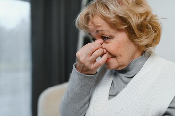 Upset older woman massaging temples touching aching head feeling strong headache or migraine...