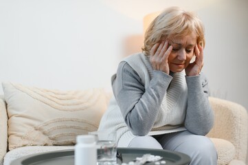 Upset older woman massaging temples touching aching head feeling strong headache or migraine...
