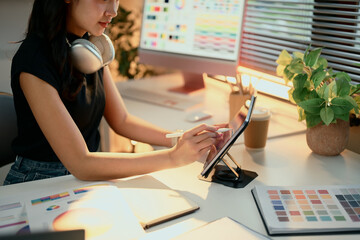 Cheerful graphic designer working on digital tablet in a creative studio with color palettes on...