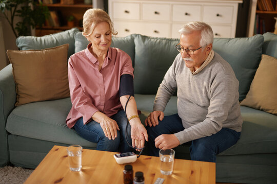 In a cozy living room, an elderly couple engages in a health check, with one partner measuring blood pressure while the other observes and assists, fostering care and togetherness.
