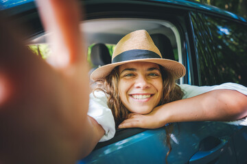 Portrait of happy young woman in hat traveling by car, selfie summer vacation and travel concept