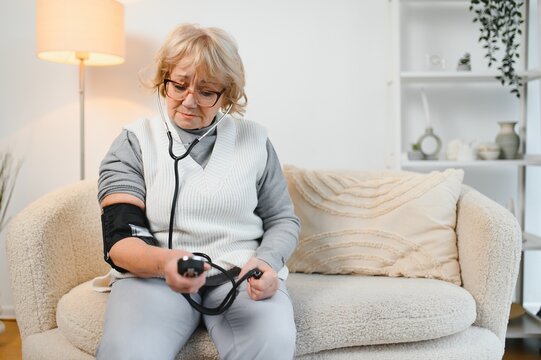 Senior woman with hypertension measuring blood pressure herself at home. Mature lady measure blood pressure using tonometer.