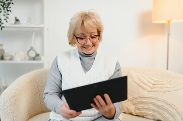 Head shot portrait close up happy mature woman using computer tablet, looking at camera, laughing...