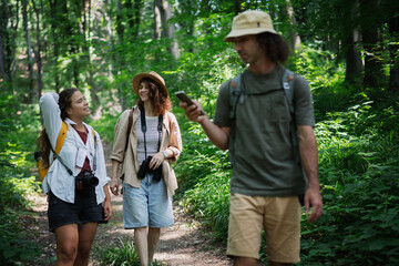 Group of happy young people friends hiking with camera binoculars and backpacks , walking in summer forest