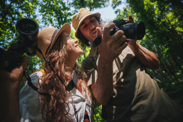 Young happy couple with photo camera and binoculars walking hiking in summer forest