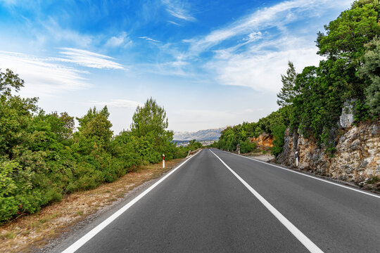 An expansive view of an empty, well-maintained highway winding through a lush, green landscape under a bright, perfect for conveying themes of travel, freedom, and natural beauty.