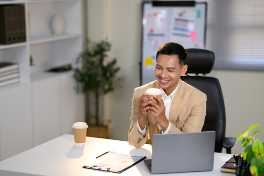Confident businessman holding a coffee cup and reviewing documents in a modern office