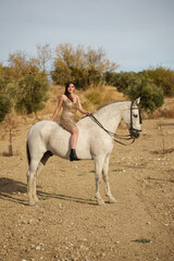Young girl in a beautiful dress riding a white horse in the countryside at sunset