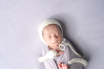 A professional newborn photo shows a half-month-old Japanese baby sleeping in a soft wrap. The baby wears a white knitted hat. A zodiac snake plush is curled beside them on a pale purple background.