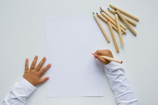 Child drawing on blank paper with colored pencils on white background