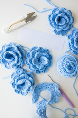 Blue crochet flowers and yarn with tools on white surface