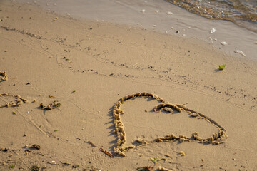 heart drawn with a stick on the wet sand of a lakeside beach. Gentle waves approach the shore, creating a romantic summer scene