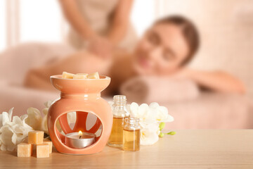 Spa therapy. Woman receiving massage on table and composition with aroma lamp in salon, selective focus