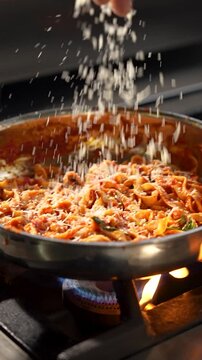 grated cheese, getting added in a pan with red sauce pasta while preparation