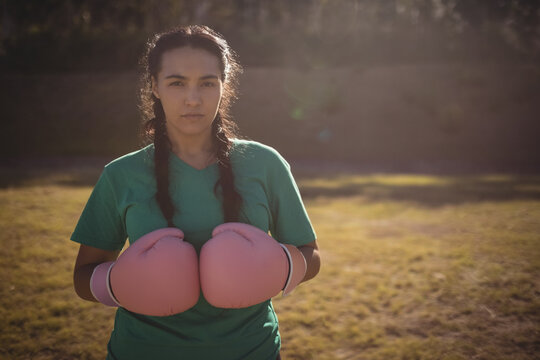 Fototapeta Female athlete is wearing green shirt, holding pink boxing gloves in sunlit field with long shadows