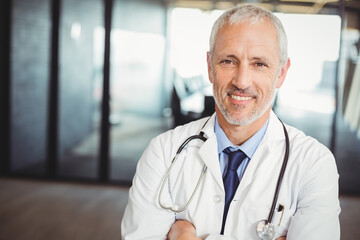 Doctor standing in glass-partitioned corridor, wearing lab coat with stethoscope and pen