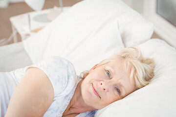Woman reclining on bed with floral nightshirt, resting head on white pillow near bedside lamp