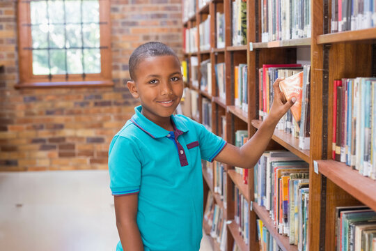 African American boy reaching for book on bookshelf in library aisle by brick multi-pane window