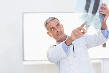 Male doctor in lab coat reading X-ray film on lightbox in clinic with stethoscope, copy space